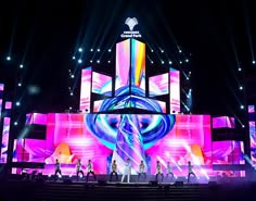 a group of people standing on top of a stage under bright colored lights at night