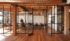 a person sitting at a table in an open room with glass walls and wooden floors