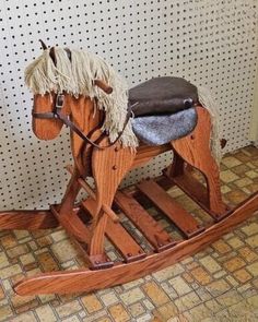 a wooden rocking horse with a saddle on it's back, sitting in front of a wall