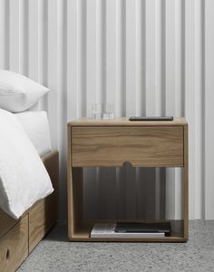 a bed with white sheets and pillows next to a wooden night stand on the floor