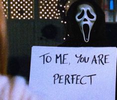 a person wearing a ghost mask holding a sign that says to me, you are perfect