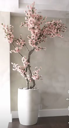 a bonsai tree with pink flowers in a white pot on a table next to a wall