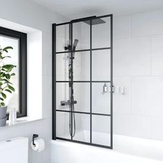 a bathroom with a white toilet and black framed shower enclosure next to a bathtub