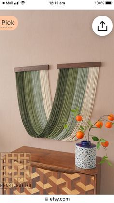 an orange vase sitting on top of a wooden dresser next to a wall hanging with two green and white curtains