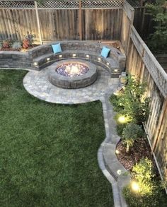 an outdoor fire pit surrounded by green grass and landscaping lighting up the area around it