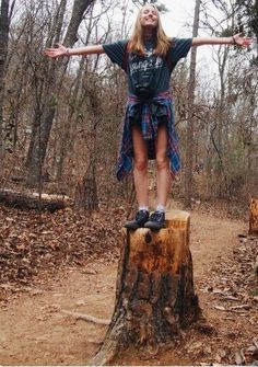 a young woman standing on top of a tree stump in the middle of a forest