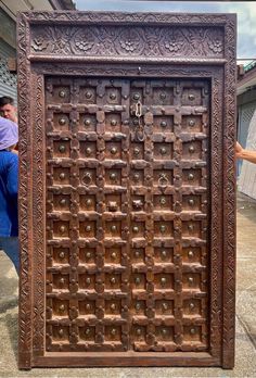 an old wooden door with intricate carvings on the front and sides, is being held up by a woman