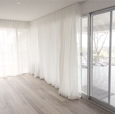 an empty room with white curtains and wood flooring on the outside, looking out onto a patio