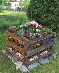 a wooden planter filled with lots of flowers in the grass next to some rocks