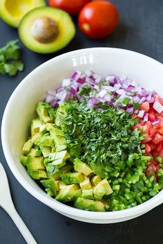 a bowl filled with chopped up vegetables next to avocado and tomatoes