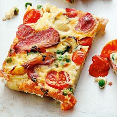 two slices of pizza on a cutting board with tomatoes and other toppings next to it