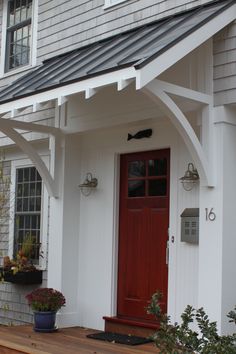 a white house with a red door and some plants on the front porch, next to it is a potted plant