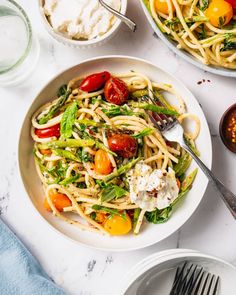 a white plate topped with pasta and veggies next to bowls of dips