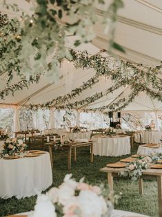 tables and chairs are set up in a tent for an outdoor wedding reception, with greenery hanging from the ceiling