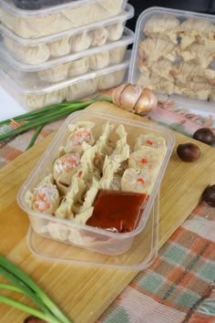 some food is sitting in plastic containers on a wooden board next to garlic and other foods