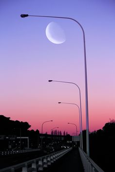 the sun is setting over an empty street with traffic lights and street lamps on either side