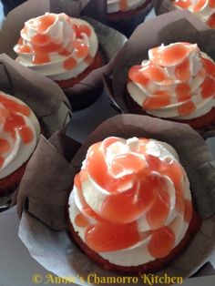 cupcakes with orange icing and white frosting on top are sitting in brown paper wrappers