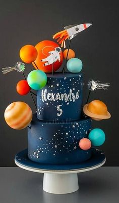 a blue cake with planets and rockets on top, sitting on a white pedestal in front of a black background