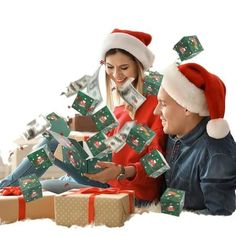 a man and woman sitting on the floor with presents in front of them, both wearing santa hats