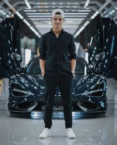 a man standing in front of a black sports car with his hands on his hips