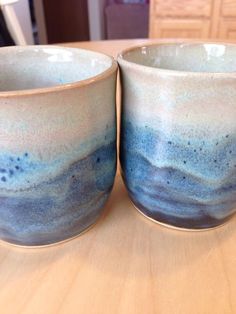 two blue and white cups sitting on top of a wooden table next to each other