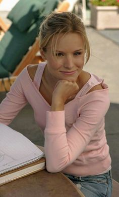 a woman sitting at a table with a notebook and pen in front of her face