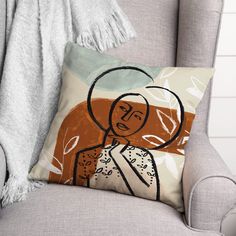 a pillow with a drawing of a woman on it sitting in a chair next to a blanket