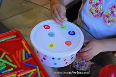 a young child is playing with an activity bucket filled with colorful beads and plastic straws