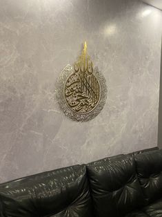 a black leather couch sitting in front of a wall with an arabic calligraphy on it