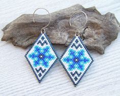 two blue and white beaded earrings sitting on top of a piece of driftwood