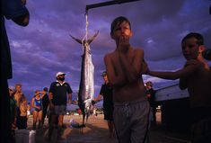 a group of people standing next to each other near a large fish on a hook