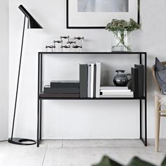 a black shelf with books and vases on it next to a chair in a white room