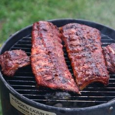 three ribs are cooking on a bbq grill outside in the grass, and there is no image here to provide a caption for