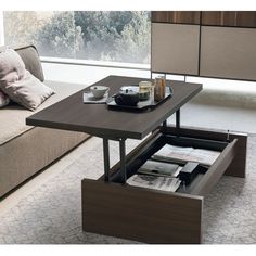 a coffee table with an open drawer underneath it in front of a couch and window