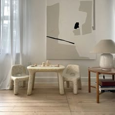 a white table and two chairs in front of a large art piece on the wall