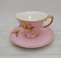 a pink cup and saucer with gold flowers on it