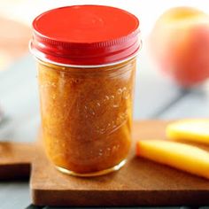 a jar filled with peanut butter sitting on top of a wooden cutting board next to an apple