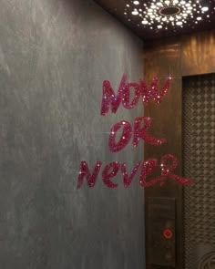 the words now or never are spelled with pink sparkles in front of a gray wall