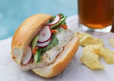 a sandwich and chips on a napkin next to a glass of beer with water in the background