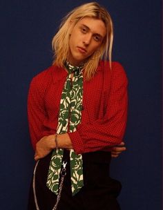 a woman with blonde hair wearing a red shirt and green neck tie standing in front of a blue wall