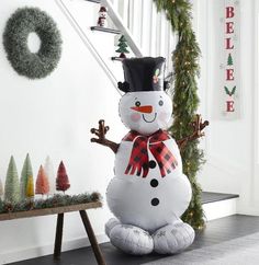 an inflatable snowman sitting on the ground next to christmas trees and wreaths