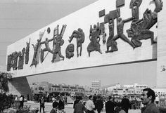 black and white photograph of people walking in front of a building with chinese characters on it