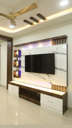 a living room with white marble walls and ceiling fan in the center, along with a flat screen tv mounted on an entertainment unit