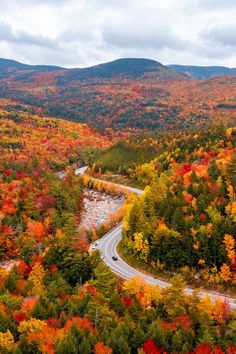 a winding road surrounded by colorful trees in the fall with mountains in the back ground