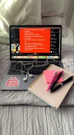 a laptop computer sitting on top of a bed next to a notepad and pen