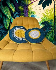 a yellow chair with two crocheted pillows on it in front of a tropical wall