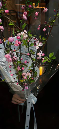 a person holding a bouquet of flowers in front of a glass window with a lit candle