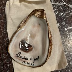 a white and gold shell with a wedding date on it sitting on a cloth bag