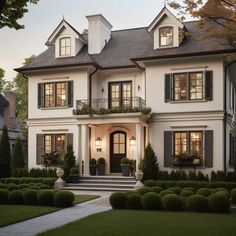 a large white house with lots of windows and bushes in front of the entrance to it