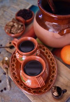 two cups of coffee sit on a plate next to some oranges and spoons